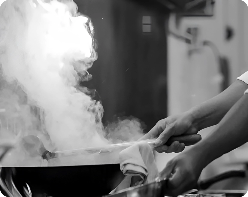 A person cooking with a wok, creating a large plume of steam or smoke.