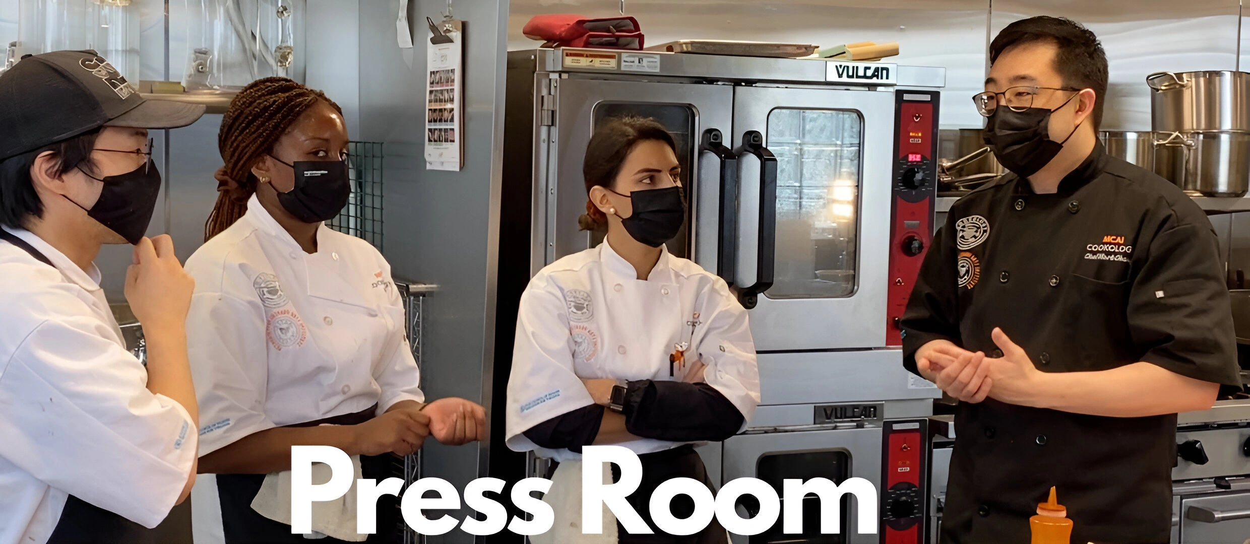 Four chefs in a kitchen wearing masks and uniforms, standing near ovens. One chef is speaking while the others listen. Text on image reads "Press Room.