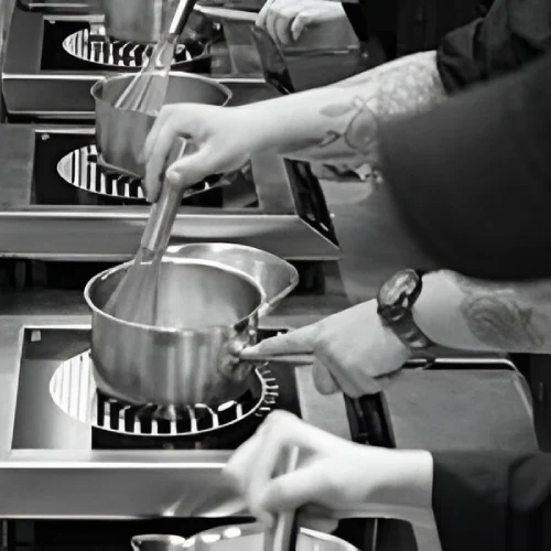 Several people stir pots on a stove in a kitchen, focusing on cooking tasks.